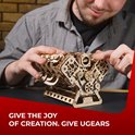 Man monteert een houten V8-motor model, terwijl hij glimlacht. Tekst: GIVE THE JOY OF CREATION. GIVE UGEARS.