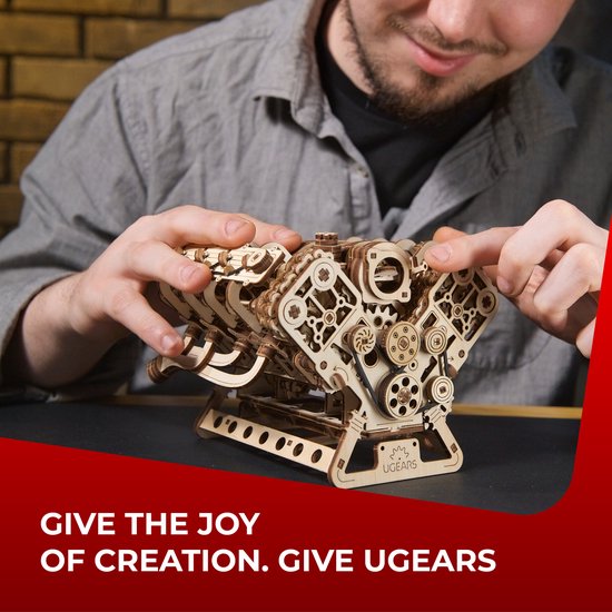 Man monteert een houten V8-motor model, terwijl hij glimlacht. Tekst: GIVE THE JOY OF CREATION. GIVE UGEARS.