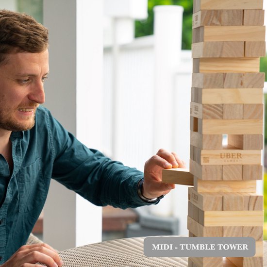 Man in donkerblauwe blouse trekt blok uit grote houten stapeltoren. 'UBER GAMES' logo's zichtbaar.