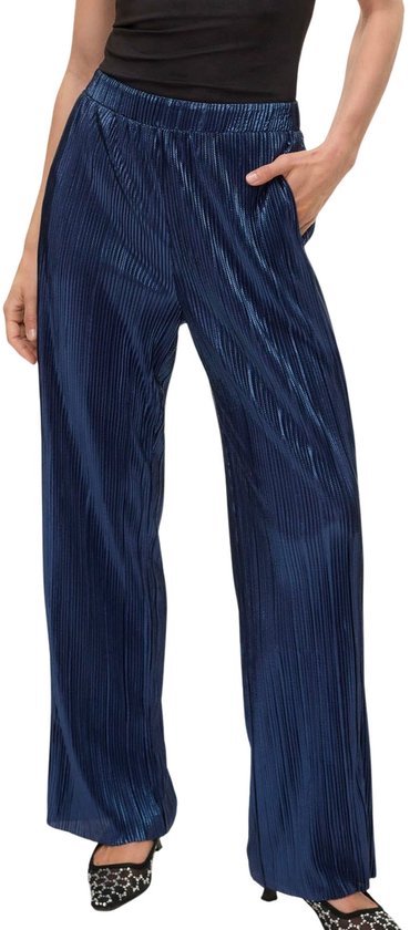 Model in een donkerblauwe, glanzende, wijde broek met plooien. Hand in de steekzak.