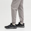 Close-up van een grijze joggingbroek met strakke broekspijpen en zwarte sneakers met witte accenten.