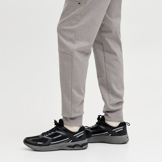 Close-up van een grijze joggingbroek met strakke broekspijpen en zwarte sneakers met witte accenten.