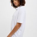 Vrouw met krullend haar, draagt een wit poloshirt, profiel.
