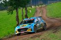 Een blauwe rallyauto met gele accenten en diverse logo's, waaronder KROON OIL, op een modderig bospad.