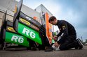 Een monteur met een overall werkt aan de grote groene en zwarte achtervleugels van een racewagen.