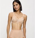 Een vrouw met een korte bob draagt een beige kanten beha en hoge bikinislip. Ze leunt tegen een muur.