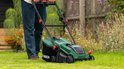 Man maait gras met groene Bosch grasmaaier in een tuin.