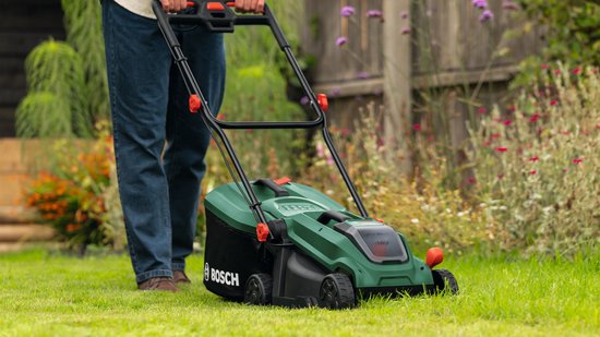 Man maait gras met groene Bosch grasmaaier in een tuin.