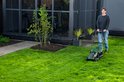 Vrouw maait gras met groene Bosch grasmaaier in een tuin.