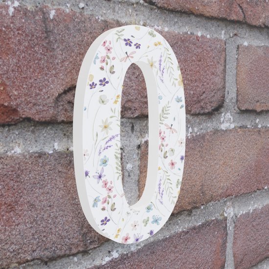 Wit huisnummer 0 met delicate bloemenprint, bloemen en libellen in pastelkleuren op een bakstenen muur.