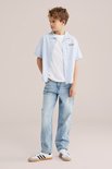 Jongen in een lichtblauwe gestreepte korte mouw overhemd en lichte jeans.