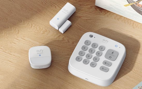 Witte Eufy beveiligingsset met keypad, bewegingssensor en deur-/raamsensoren op een houten ondergrond.
