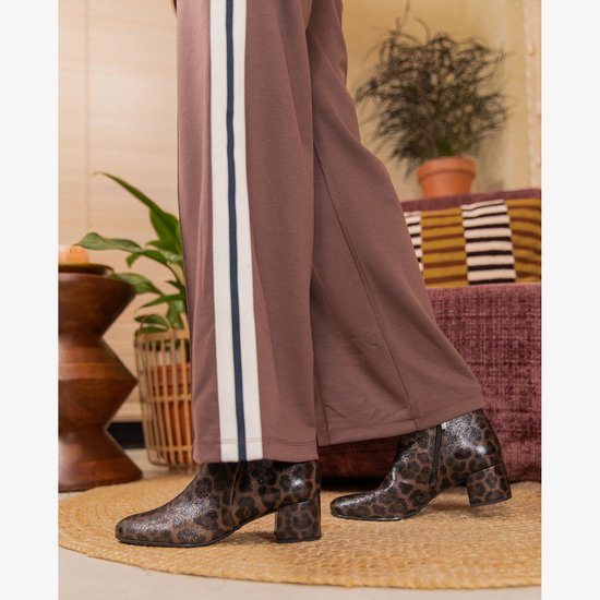 Een model draagt zwarte enkellaarsjes met luipaardprint en blokhak, bij een bruine broek met witte en blauwe strepen.