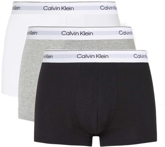 Trois trunks Calvin Klein empilés : blanc, gris et noir, chacun avec une ceinture blanche siglée.