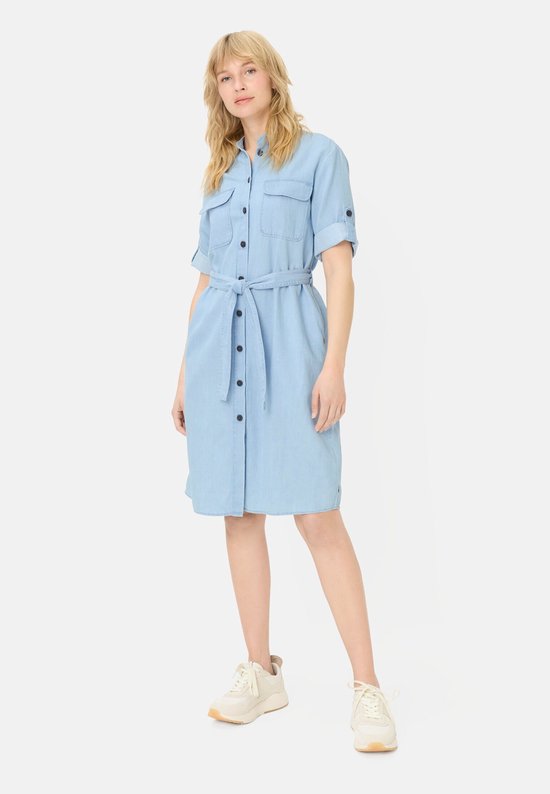 Model in een lichtblauwe spijkerjurk met korte mouwen, opgestikte borstzakken, knoopsluiting en een bijpassende stoffen ceintuur.