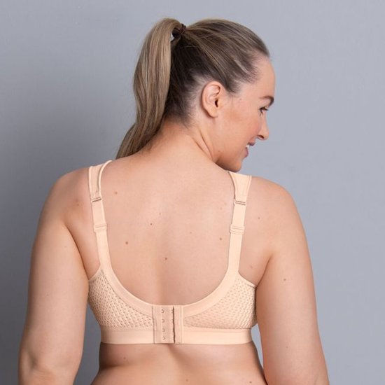Vrouw met volle figuur op de rug, draagt een beige sportbeha met geperforeerde zijkanten.