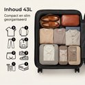 Een geopende 43L beige koffer met inhoud: kleding, schoenen en toiletartikelen.