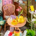 Een miniatuur theeservies in geel met gebak op een ronde tafel.