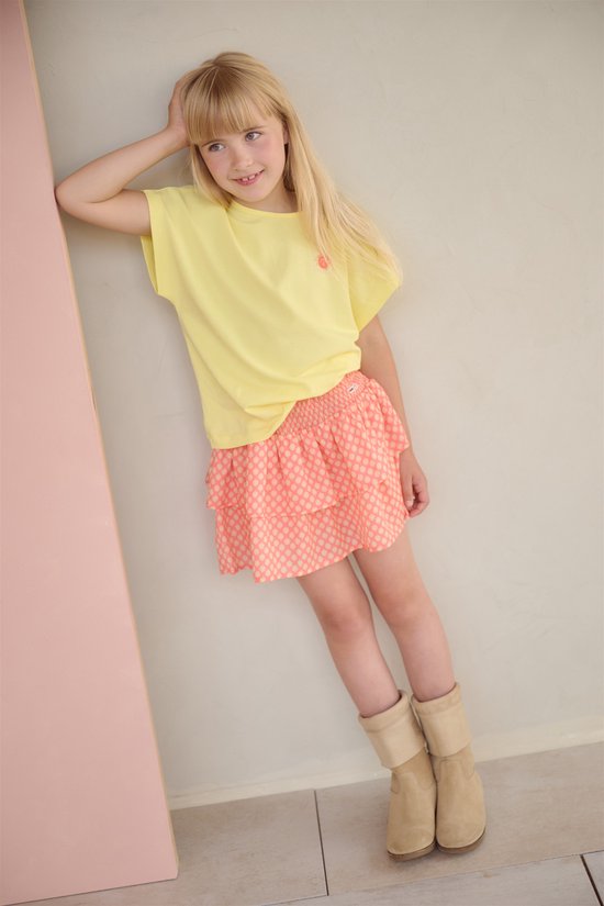 Meisje met blond haar draagt een lichtgeel T-shirt met een oranje zon-opdruk en een oranje geruite rok.