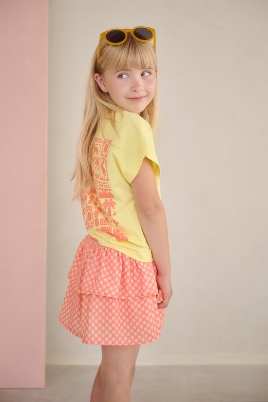 Meisje met blond haar draagt een lichtgeel T-shirt met oranje opdruk op de rug en een oranje geruite rok.