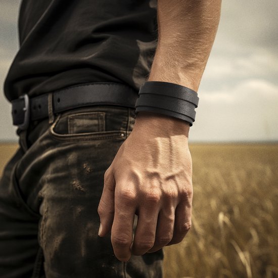 Brede zwarte leren armband om de pols van een man in een veld.