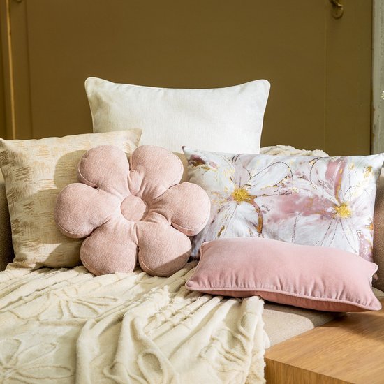 Verschillende sierkussens op een beige plaid, waaronder een roze bloemvormig kussen.