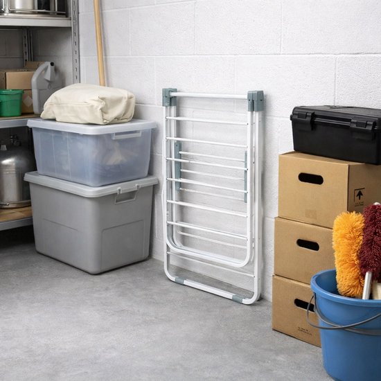 Wit inklapbaar droogrek staand op een garagevloer naast dozen en opbergbakken.