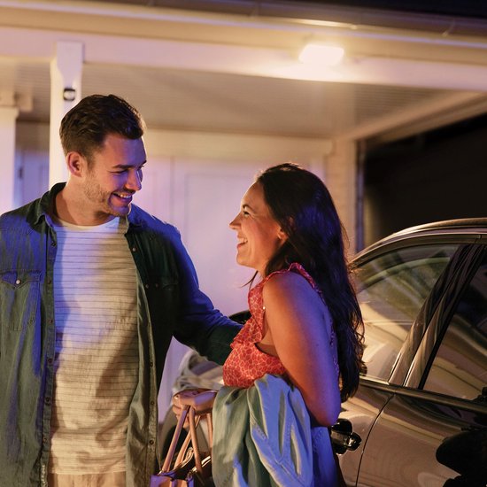 Man en vrouw lachen bij een auto onder een Philips Hue buitenlamp.