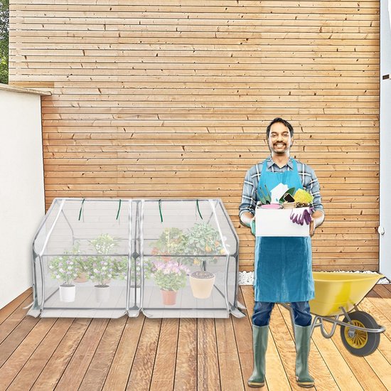 Man met schort en gereedschap naast een dubbele mini-kas met planten.