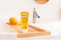 Weleda baby shampoo & douchecrème in gele tube, op een houten plankje in een wastafel met badaccessoires.