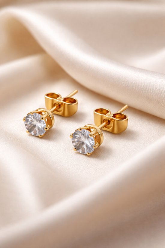 Gouden oorstekers met zirkonia steentjes op een crèmekleurige satijnen stof.