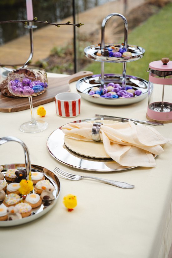 Gedekte tafel met paarse chocolade eitjes in glas en op een etagère, kleine paaskipjes en gebakjes.