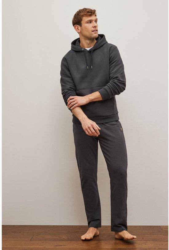 Man in een donkergrijze joggingbroek en bijpassende hoodie, kijkend naar de zijkant.