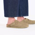 Een persoon draagt beige suède Birkenstock Boston slippers met spijkerbroek.