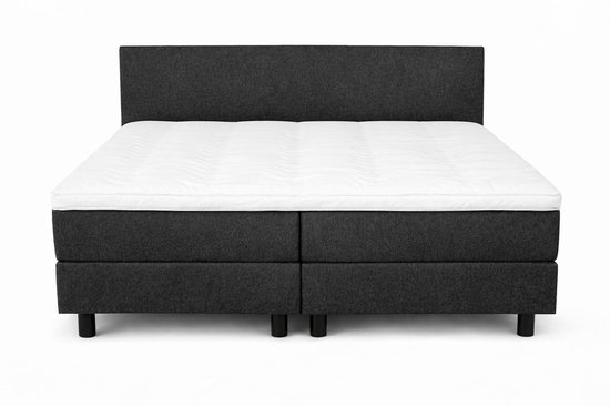 Donkergrijs gestoffeerde boxspring met wit, gegolfd matras en hoofdbord.