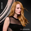 Une femme aux longs cheveux blonds brillants, regardant sur le côté. Elle porte un haut noir.