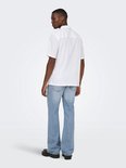 Man met witte korte mouwen blouse en lichtblauwe flared jeans, staand.