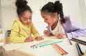 Twee meisjes met donker haar, gekleurd potlood in de hand, tekenen op papier.