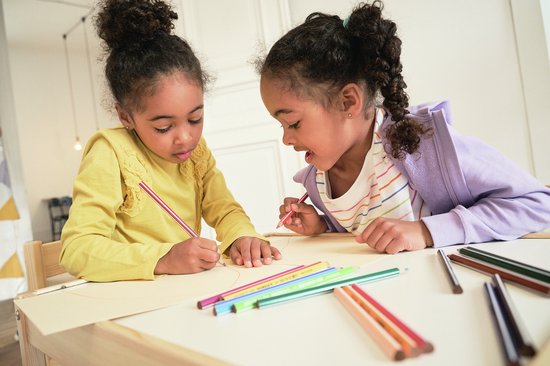Twee meisjes met donker haar, gekleurd potlood in de hand, tekenen op papier.