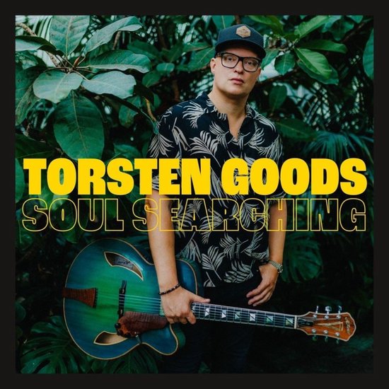 Een man met een bril en een pet draagt een zwart overhemd met palmmotief. Hij houdt een groene semi-akoestische gitaar vast. Tekst: Torsten Goods Soul Searching.