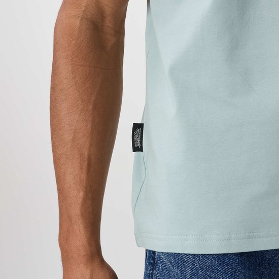 Close-up van een lichtblauwe T-shirt met een zwart label met witte tekst aan de zijkant.