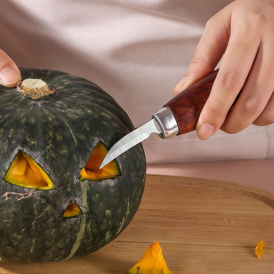 Hand met een houtsnijmes die een pompoen uitholt voor Halloween.