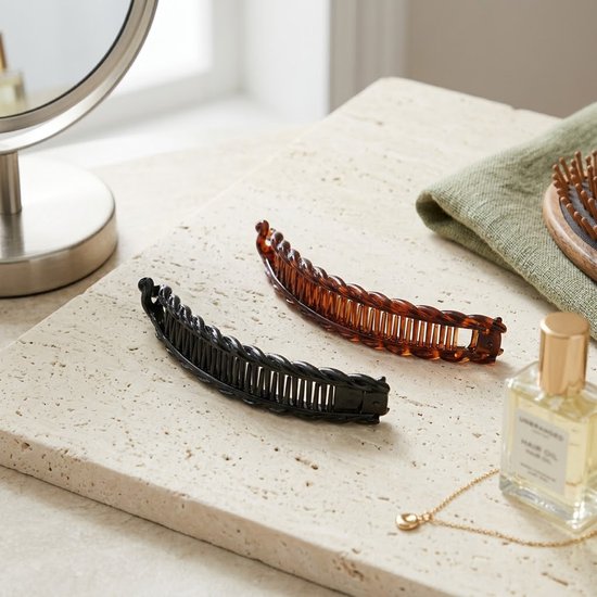 Twee gebogen haarclips, één zwart en één bruin, liggen op een stenen ondergrond.