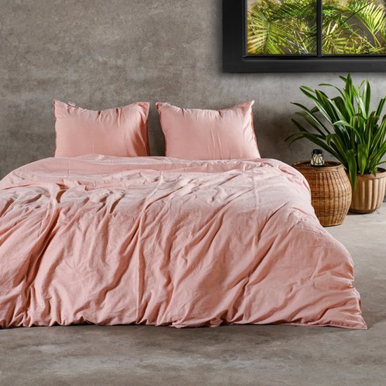 Une housse de couette rose avec deux taies d'oreiller sur un lit. Une plante se trouve à côté du lit.