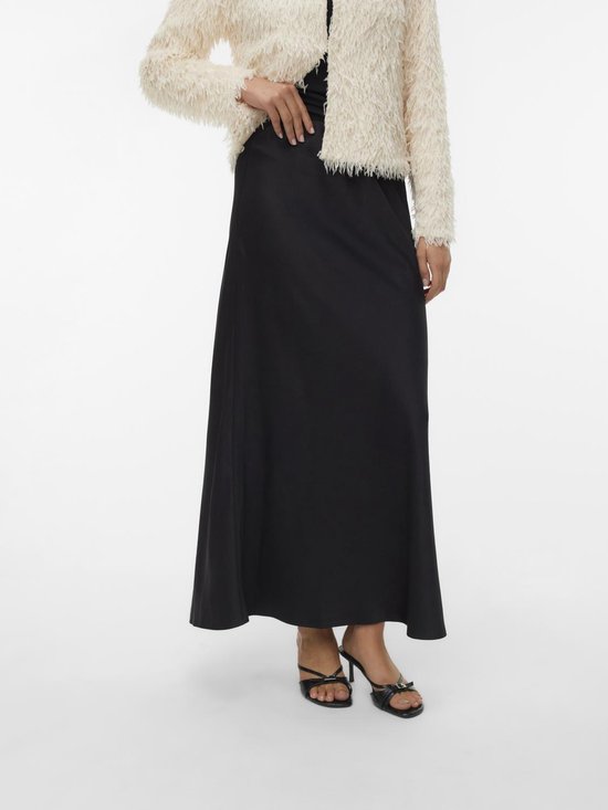 Jupe longue noire en satin portée avec une veste en tricot duveteuse blanc cassé et des sandales.