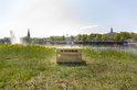 Houten Kubb kistje op gras bij een meer, met een fontein op de achtergrond.
