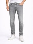 Man met grijze slim fit jeans, wit T-shirt en witte sneakers. De jeans heeft omgeslagen broekspijpen.