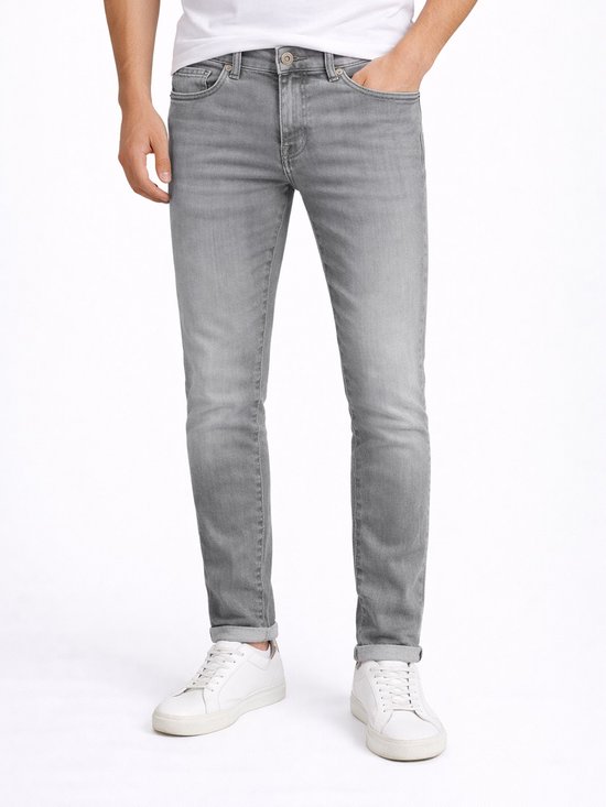 Man met grijze slim fit jeans, wit T-shirt en witte sneakers. De jeans heeft omgeslagen broekspijpen.