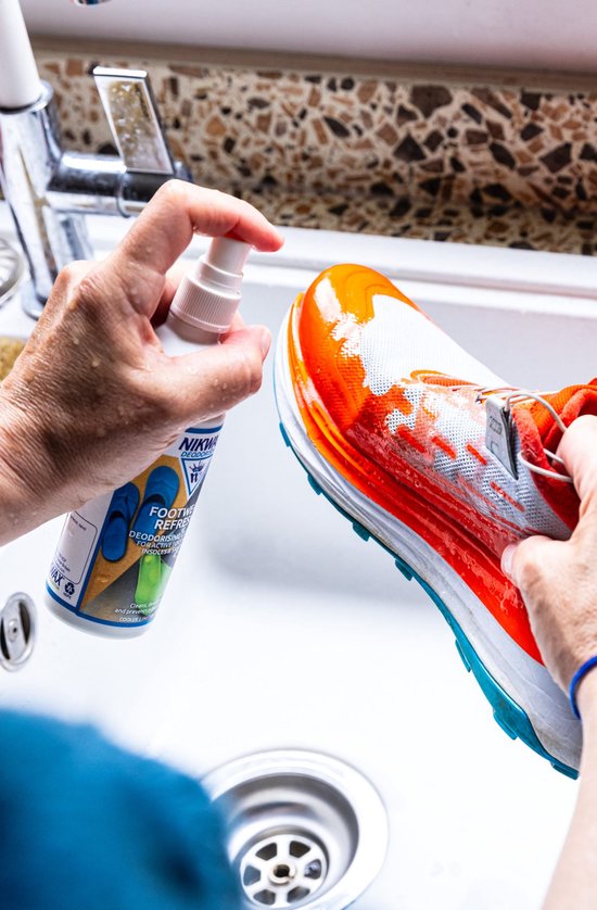Hand met blauw armbandje spuit oranje en witte hardloopschoen schoon in een gootsteen.