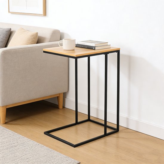 Bijzettafel met lichtbruin houtlook blad en zwart metalen C-vormig frame, naast een bank.